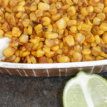 Smoked corn in a white dish with a lime wedge.